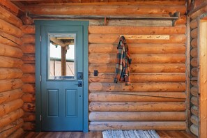 A log cabin interior with a blue door, wooden walls, and a plaid blanket hanging on the wall. - Sapphire Ridge Cabin (Hamilton)