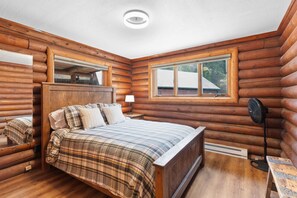 A log cabin bedroom with a wooden bed, a nightstand, a lamp, and a window. - Sapphire Ridge Cabin (Hamilton)