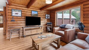 A log cabin interior with a television, sofa, coffee table, and large windows.