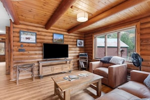A log cabin interior with a television, sofa, coffee table, and large windows. - Sapphire Ridge Cabin (Hamilton)