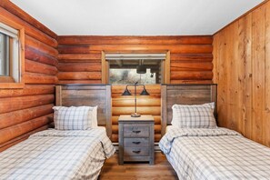 A log cabin bedroom with two beds, a nightstand, and a window.