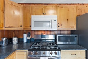 A kitchen with wooden cabinets, a gas stove, a microwave, and a toaster.