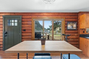 A log cabin interior with a large wooden table, a potted plant, and a telescope.