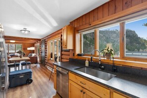 A log cabin interior with a kitchen, dining area, and a view of a mountainous landscape.
