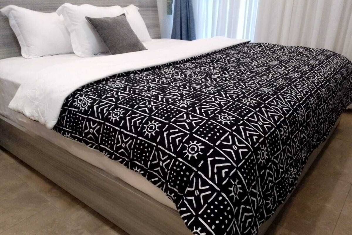 Ein Bett mit einer gemusterten Tagesdecke, einem weißen Kissen und einem grauen Kissen.