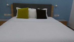 A bed with a white bedspread and three pillows in different colors. - Hôtel-228 (Lomé)