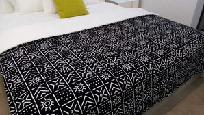 A bed with a patterned bedspread, a white pillow, and a green pillow. - Hôtel-228 (Lomé)