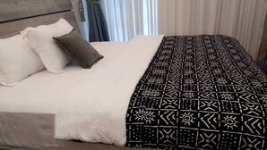 A bed with a patterned bedspread, pillows, and a wooden headboard. - Hôtel-228 (Lomé)
