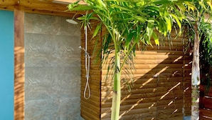 A wooden cabin with a stone wall, a shower, and a palm tree. - Luxury villa with sea view (Les Anses-d'Arlet)