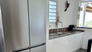 A modern kitchen with a stainless steel refrigerator, white cabinets, a sink, and a window with blinds. - Luxury villa with sea view (Les Anses-d'Arlet)