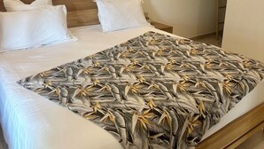 A bed with white linens and a leaf-patterned blanket, a wooden headboard, and a wall-mounted heart decoration. - Luxury villa with sea view (Les Anses-d'Arlet)