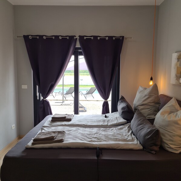 Une chambre avec un lit, des oreillers et une vue sur l’espace piscine.