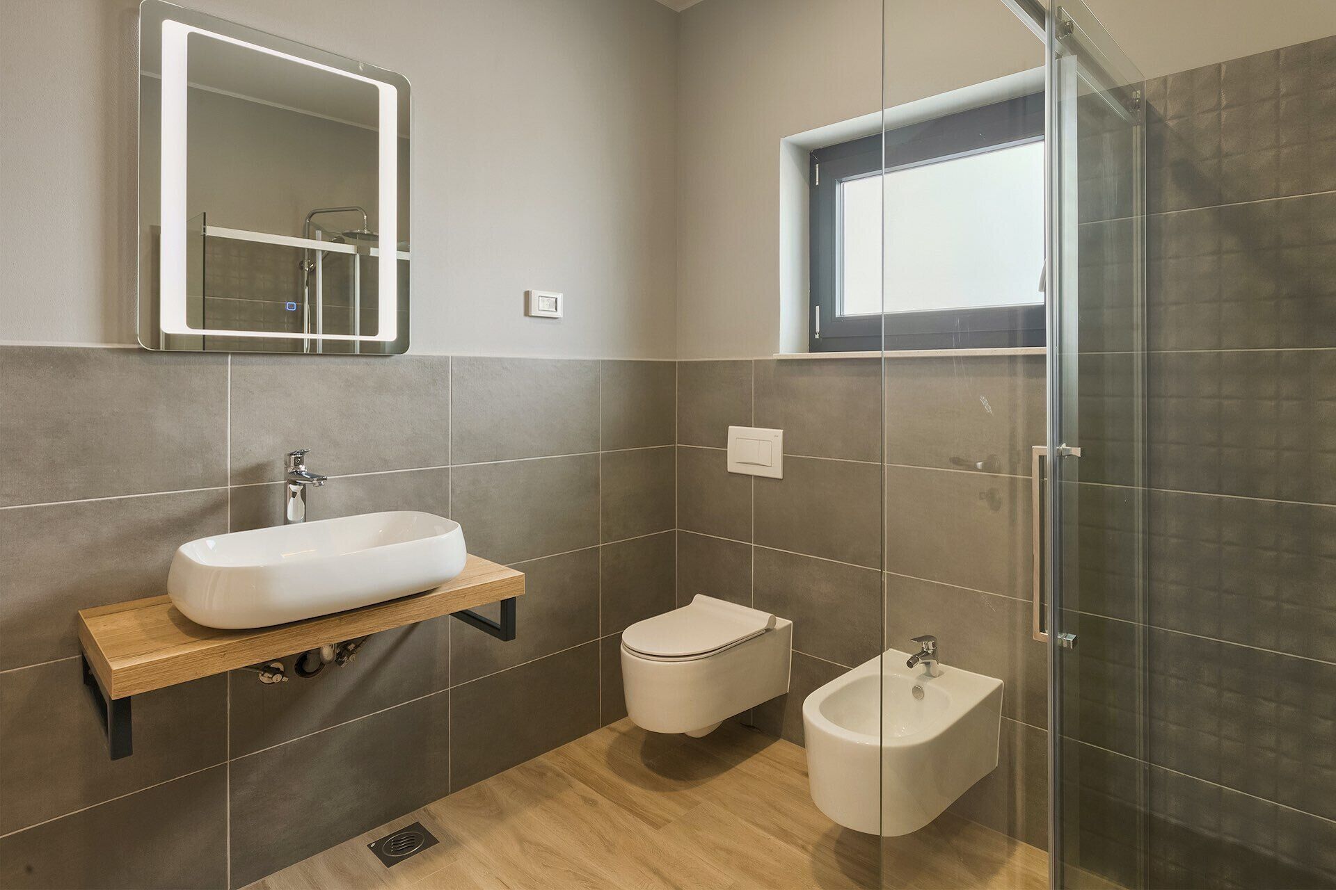 Un baño moderno con un espejo grande, un lavabo, un inodoro y un bidé.