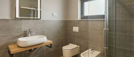 Un baño moderno con un espejo grande, un lavabo, un inodoro y un bidé.