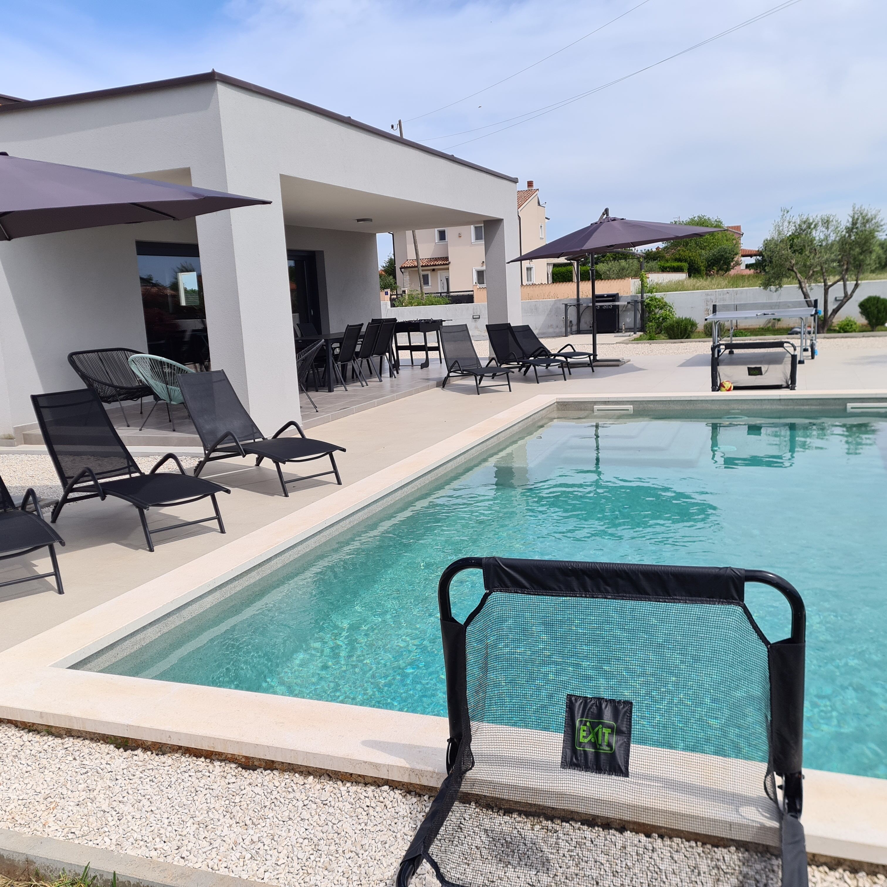 Zona de piscina amb gandules i ombrelles, una zona de seients coberta i una piscina nítida.