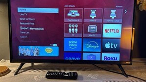 En TCL Roku-TV som visar en startsida med olika streamingtjänster och en fjärrkontroll som ligger på en vävd matta.