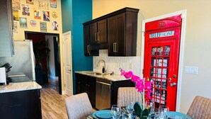 A dining area with a table set for six, a red telephone booth, and a kitchen with dark cabinets. - Xquisite Nook, the ideal getaway in Daphne, AL! (Daphne)