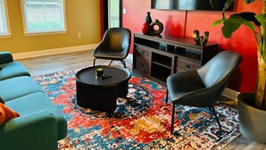 A living room with a sofa, two chairs, a coffee table, a TV, and a large plant. - Xquisite Nook, the ideal getaway in Daphne, AL! (Daphne)