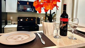 Cucina con mobili bianchi, piano cottura nero e forno a microonde. Sul bancone, un vaso con fiori arancioni, una bottiglia di vino e due bicchieri da vino.