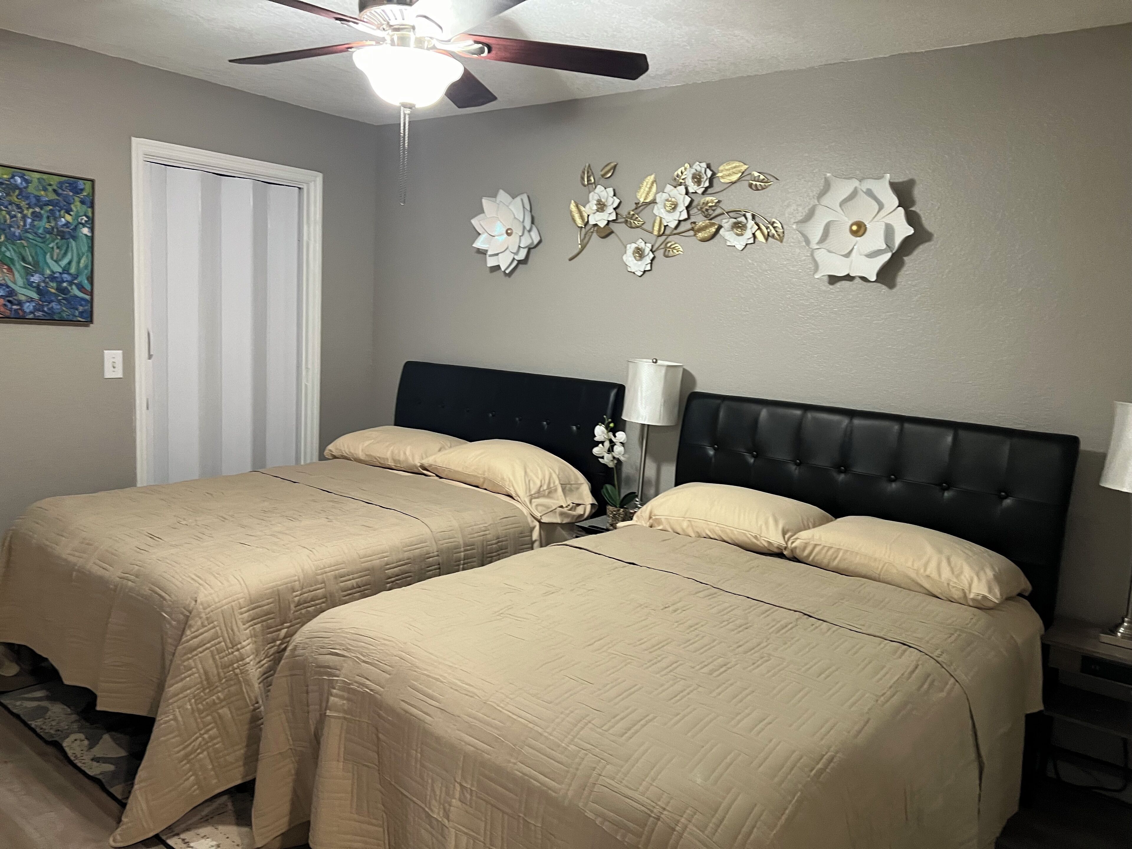 Un dormitorio con dos camas, un ventilador de techo, decoración en la pared y una puerta.