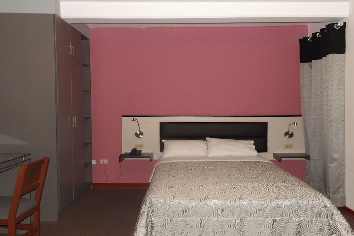 A bedroom with a bed, a desk, and a chair.