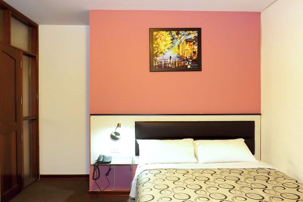 A hotel room with a bed, a nightstand, a telephone, and a painting on the wall.