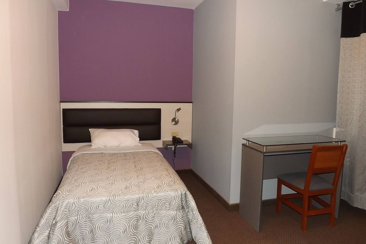 A small, compact room with a bed, a desk, and a chair.