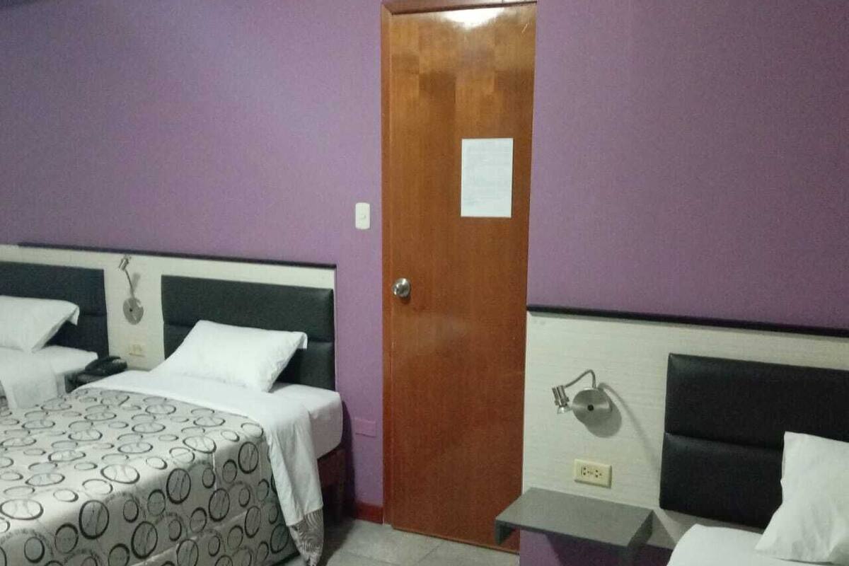 A hotel room with two beds, each with patterned bedding, a wooden door, and a small bedside table with a lamp.
