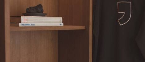 A wooden wardrobe with a hanging rack, shelves with books, and a small plant.