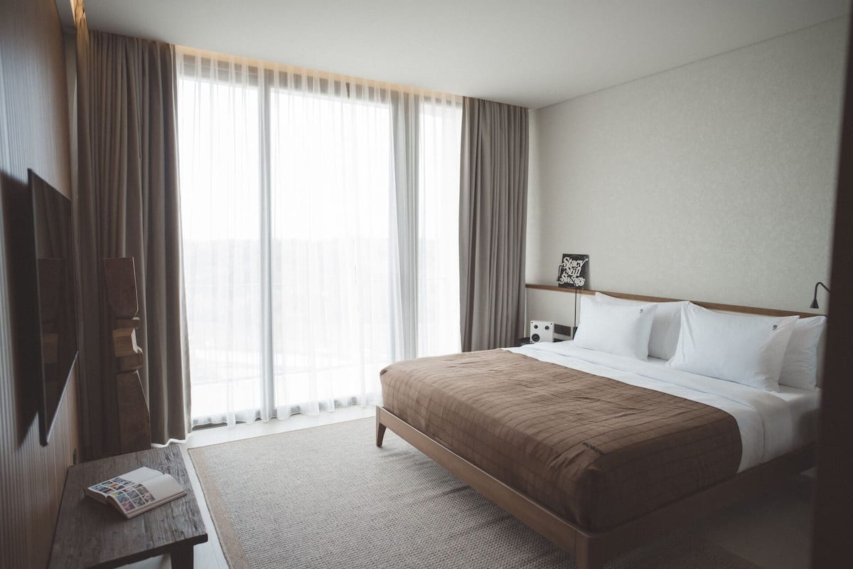A hotel room with a large bed, a bedside table, a TV, and a window with curtains.