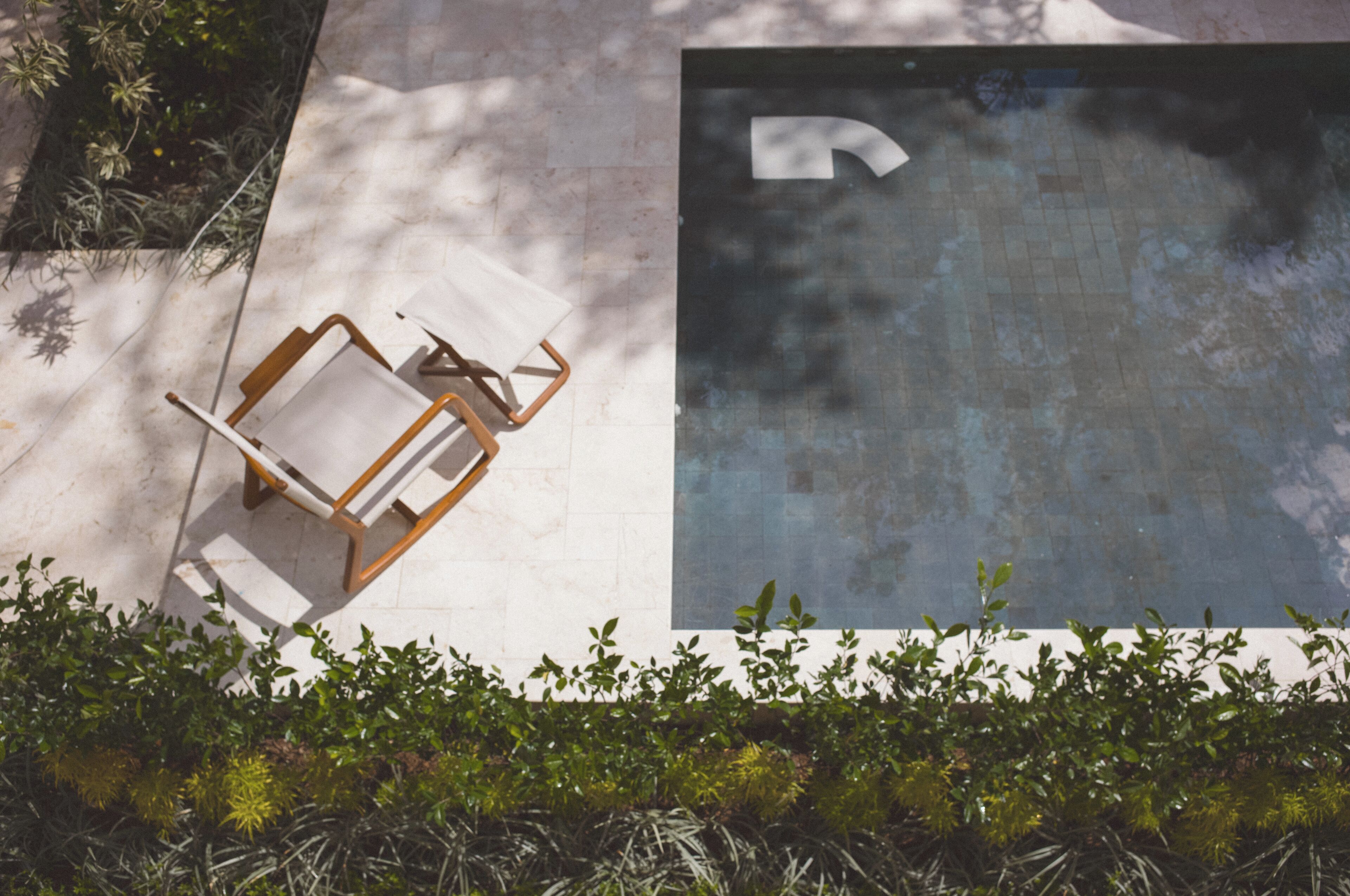 A pool area with a chair and a small table, surrounded by greenery.