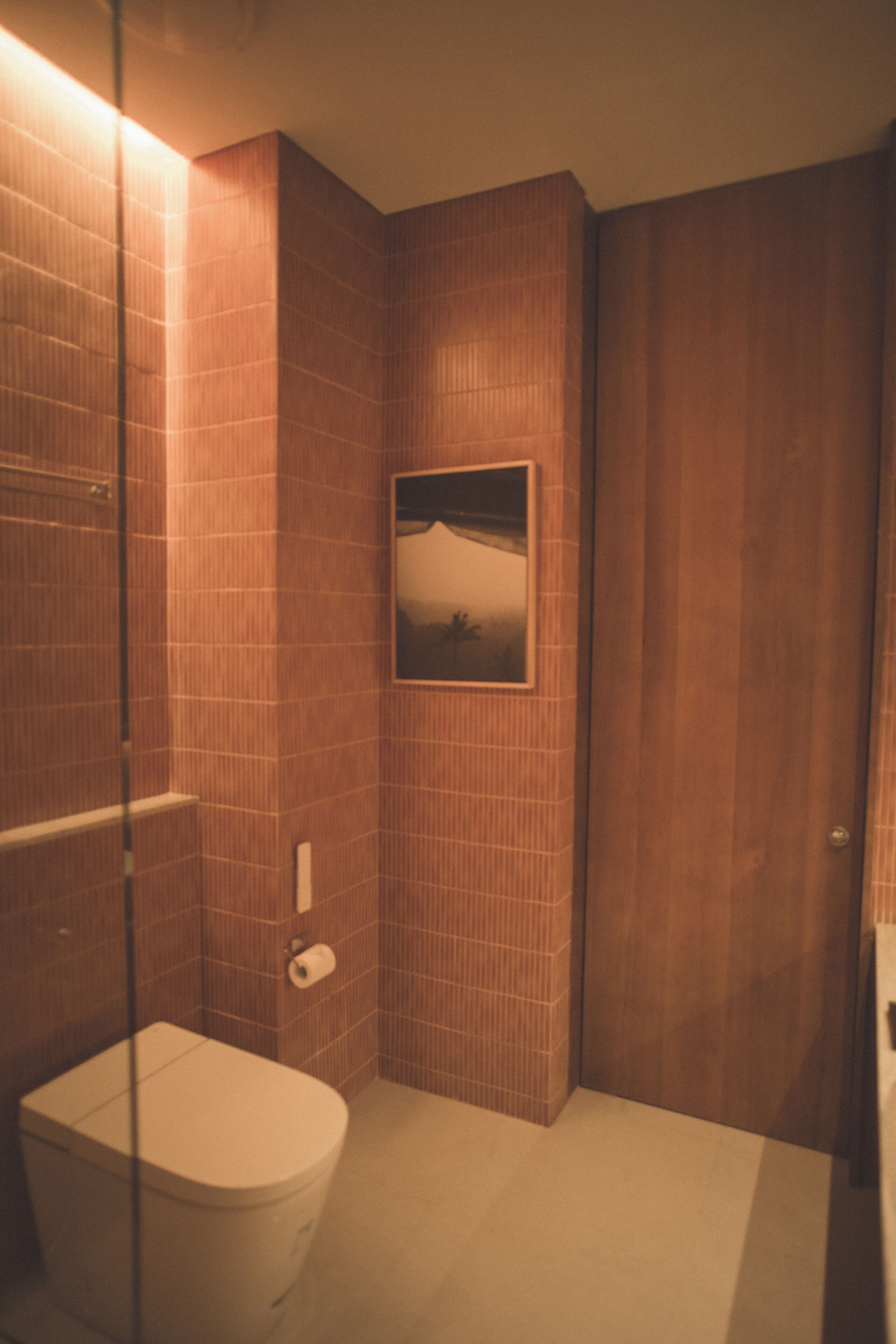 A bathroom with a toilet, a glass shower enclosure, and a picture on the wall.