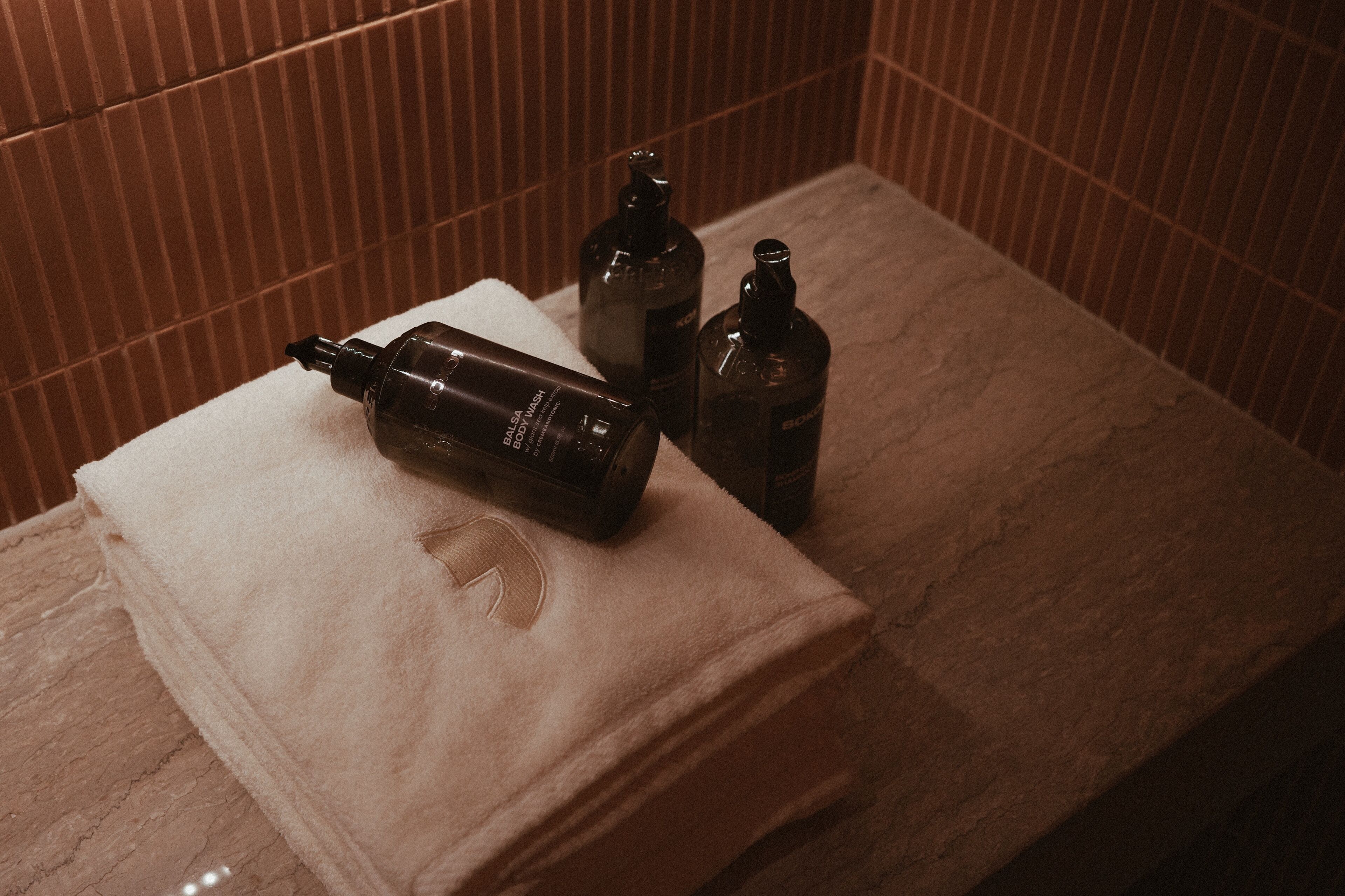 A bathroom with a towel and three bottles of body wash on a countertop.