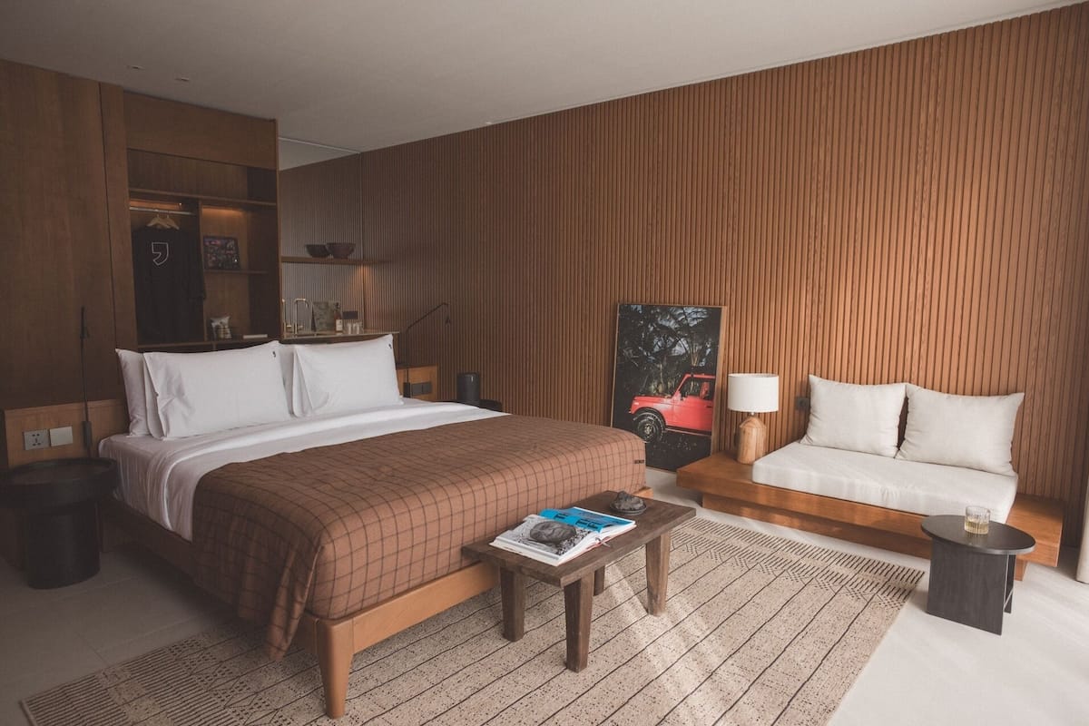 A hotel room with a large bed, a sofa, a small table, and a wooden accent wall.