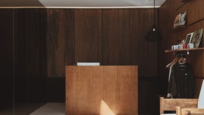 Een receptiebalie met een houten afwerking, een hangende hanglamp en een houten stoel met een kussen.