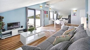A modern living room with a sofa, a coffee table, and a TV. There is a dining area with a table and chairs. - Great 3-Bedroom Apartment with Sea View (Orebic)