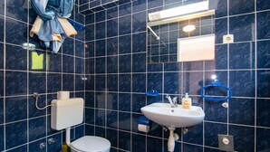 A bathroom with dark blue tiles, a white toilet, a sink with a soap dispenser, and a towel rack.