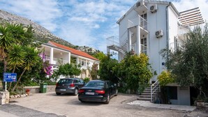 A residential building with a red-tiled roof, two cars parked in front, and a sign indicating parking availability.