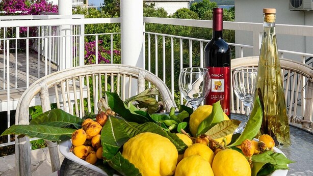A table with a plate of lemons and limes, a bottle of wine, and a glass on a balcony.