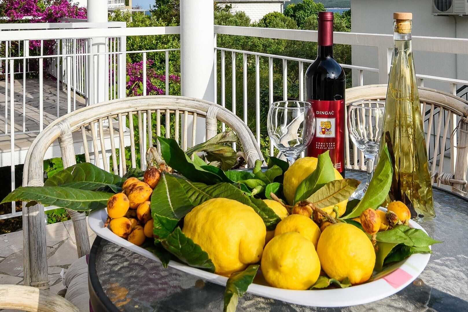 A table with a plate of lemons and limes, a bottle of wine, and a glass on a balcony.