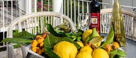 A table with a plate of lemons and limes, a bottle of wine, and a glass on a balcony.