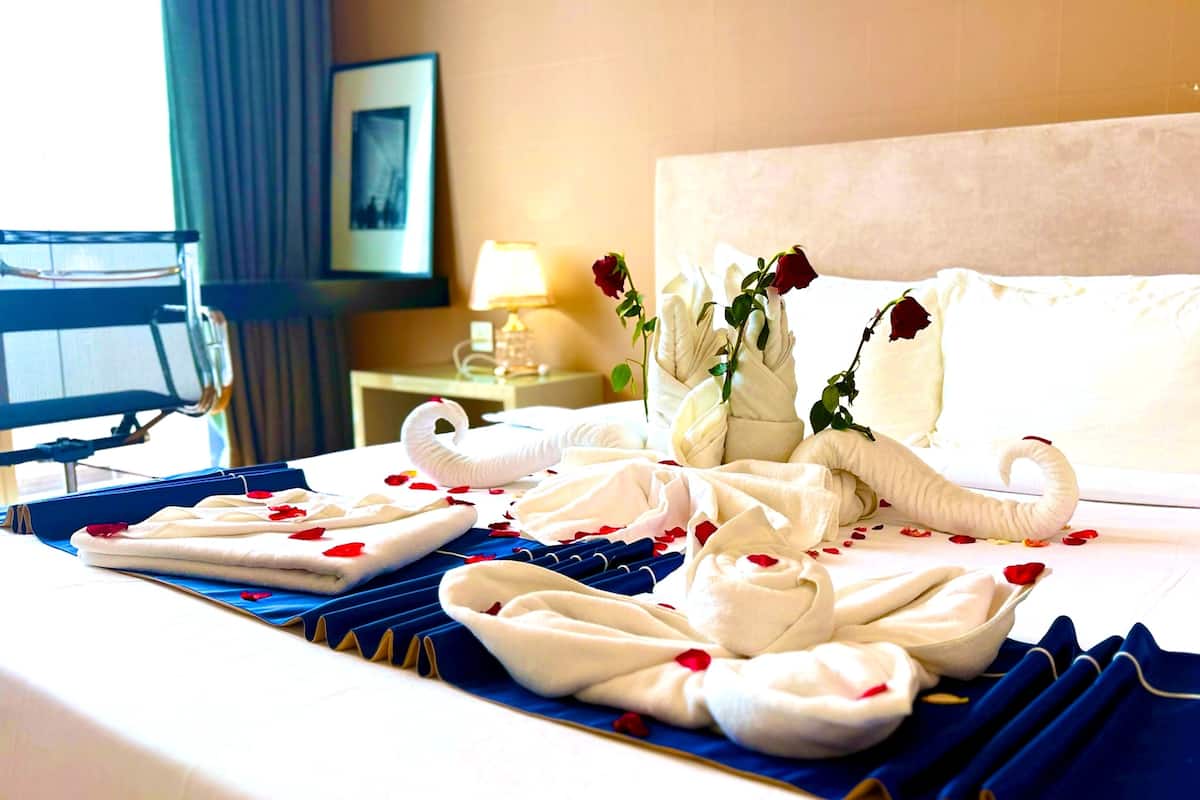 A hotel room with a neatly made bed, a vase with roses, and a swan-shaped towel arrangement.
