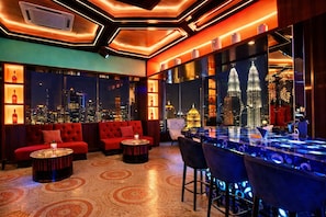 Zona de bar moderna con vista a la ciudad, asientos rojos y una barra con taburetes.