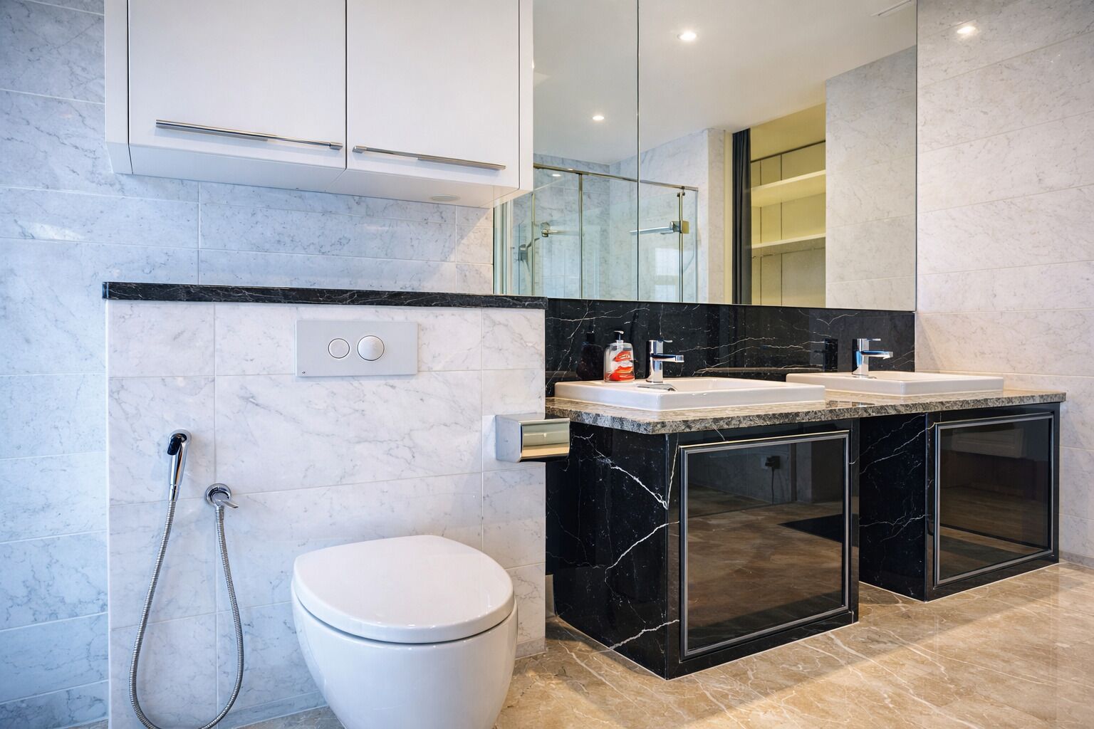 Un baño moderno con inodoro blanco, cabina de ducha de cristal, tocador de mármol negro y un espejo grande.