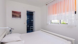 A bedroom with a bed, a window with sheer curtains, a shower with blue tiles, and a wall-mounted picture. - Great 2+2 Apartment very close to the sea. (Kuciste)