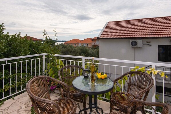 A balcony with wicker chairs and a glass table, a bottle of wine, and a bowl of fruit.