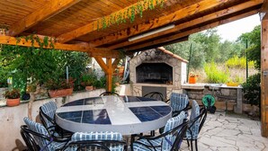 An outdoor patio with a stone fireplace, a round table, and blue plaid chairs. - Great 2+2 Apartment very close to the sea. (Kuciste)