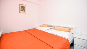 A bedroom with a single bed, white walls, a framed picture on the wall, and a white bedside table. - Great 2+2 Apartment very close to the sea. (Kuciste)