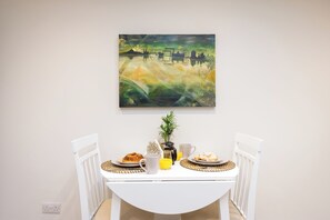 A dining area with a white table, two white chairs, and a painting on the wall. - Cosy historic cottage in Hillsborough, near Belfast, Dublin & local attractions (Royal Hillsborough)