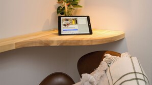 A wooden shelf with a tablet displaying a webpage, a framed document on the wall, and a plant with red flowers. - Cosy historic cottage in Hillsborough, near Belfast, Dublin & local attractions (Royal Hillsborough)